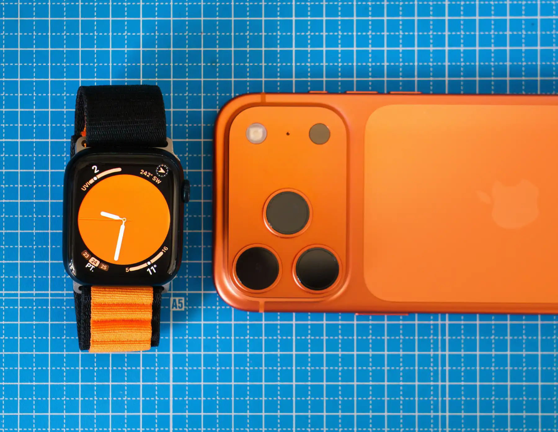 Minimalist setup featuring an orange-themed smartphone and smartwatch on a blue grid background