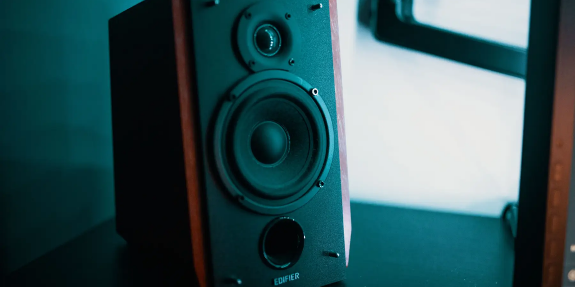 A sleek modern speaker with a wooden finish sits on a black table in a creative studio setting