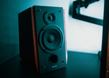 A sleek modern speaker with a wooden finish sits on a black table in a creative studio setting