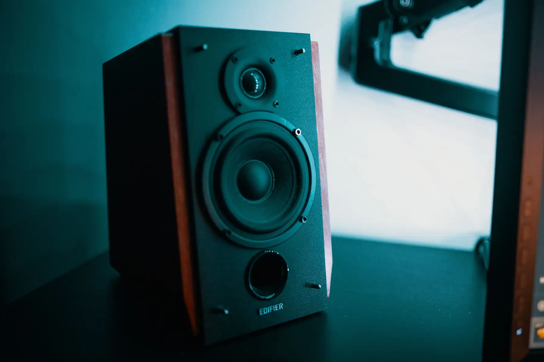 A sleek modern speaker with a wooden finish sits on a black table in a creative studio setting