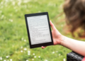 A person reads an eBook on a Kobo device while relaxing outdoors in a sunny park