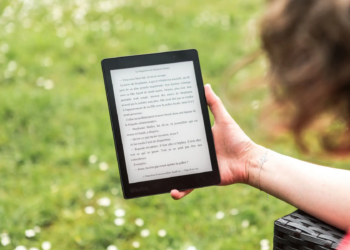 A person reads an eBook on a Kobo device while relaxing outdoors in a sunny park