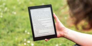 A person reads an eBook on a Kobo device while relaxing outdoors in a sunny park