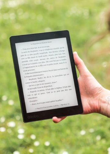 A person reads an eBook on a Kobo device while relaxing outdoors in a sunny park