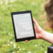 A person reads an eBook on a Kobo device while relaxing outdoors in a sunny park