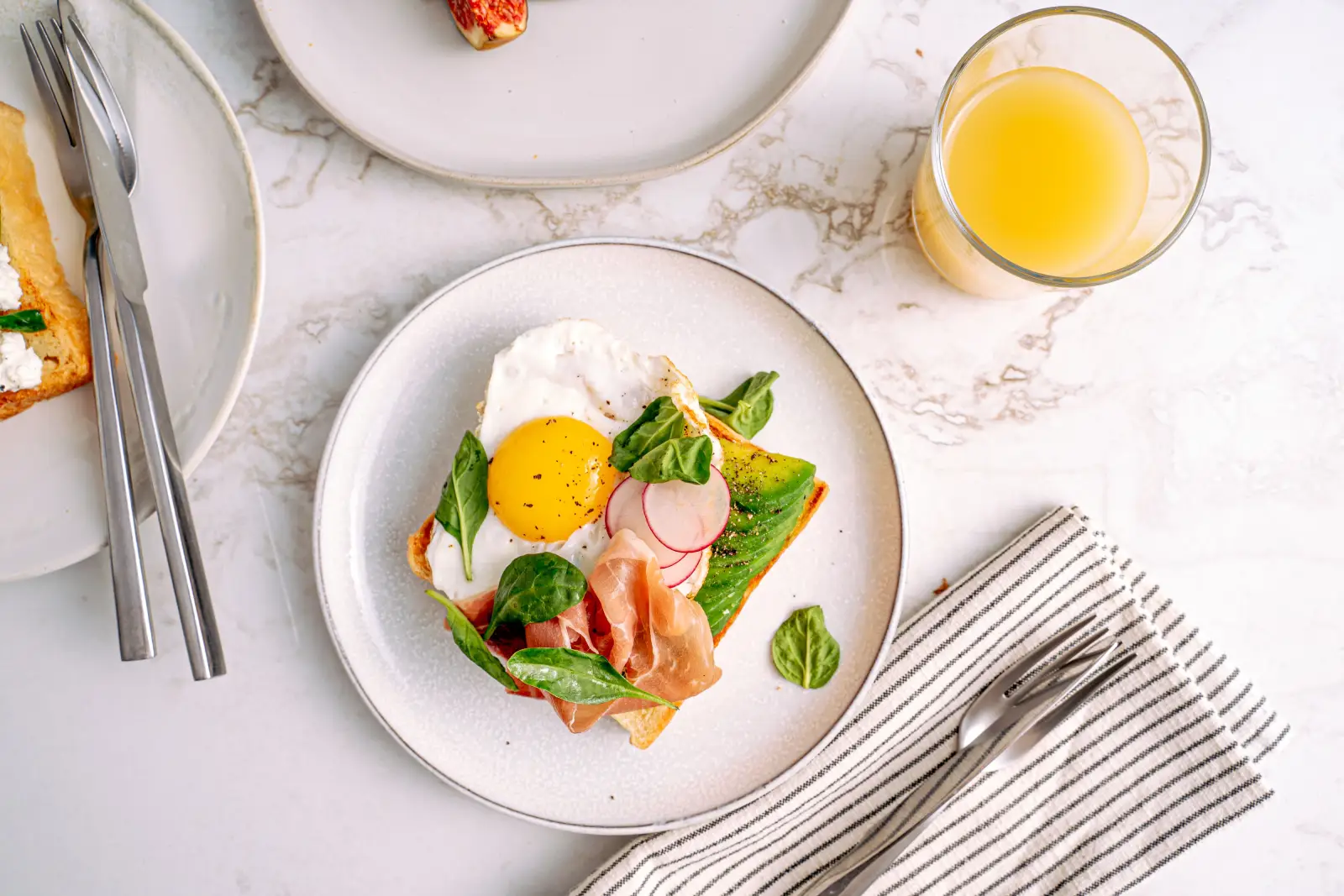 Delicious breakfast featuring avocado toast with egg and prosciutto, served with orange juice.