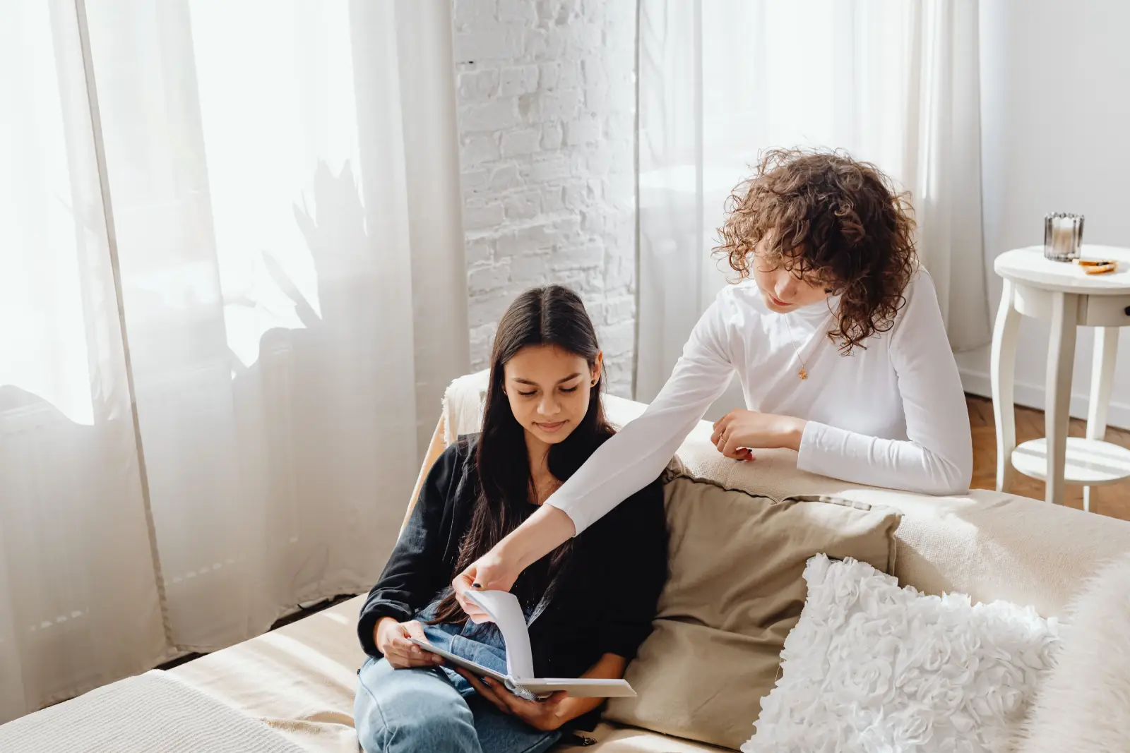 Two women enjoying a book together on a sofa in a bright, cozy living room setting