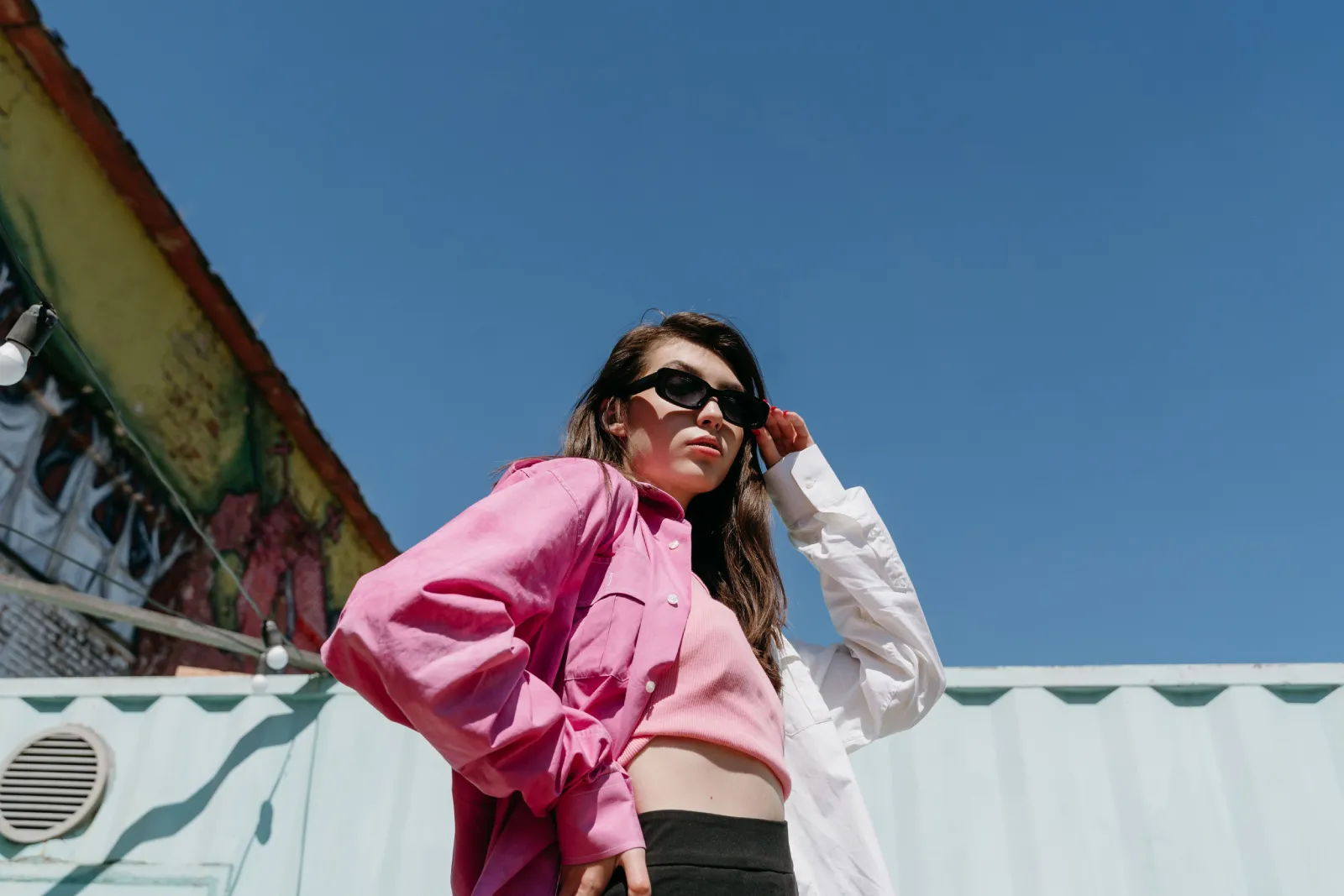 Fashion model poses confidently in pink attire against a clear blue sky, exuding modern style and confidence