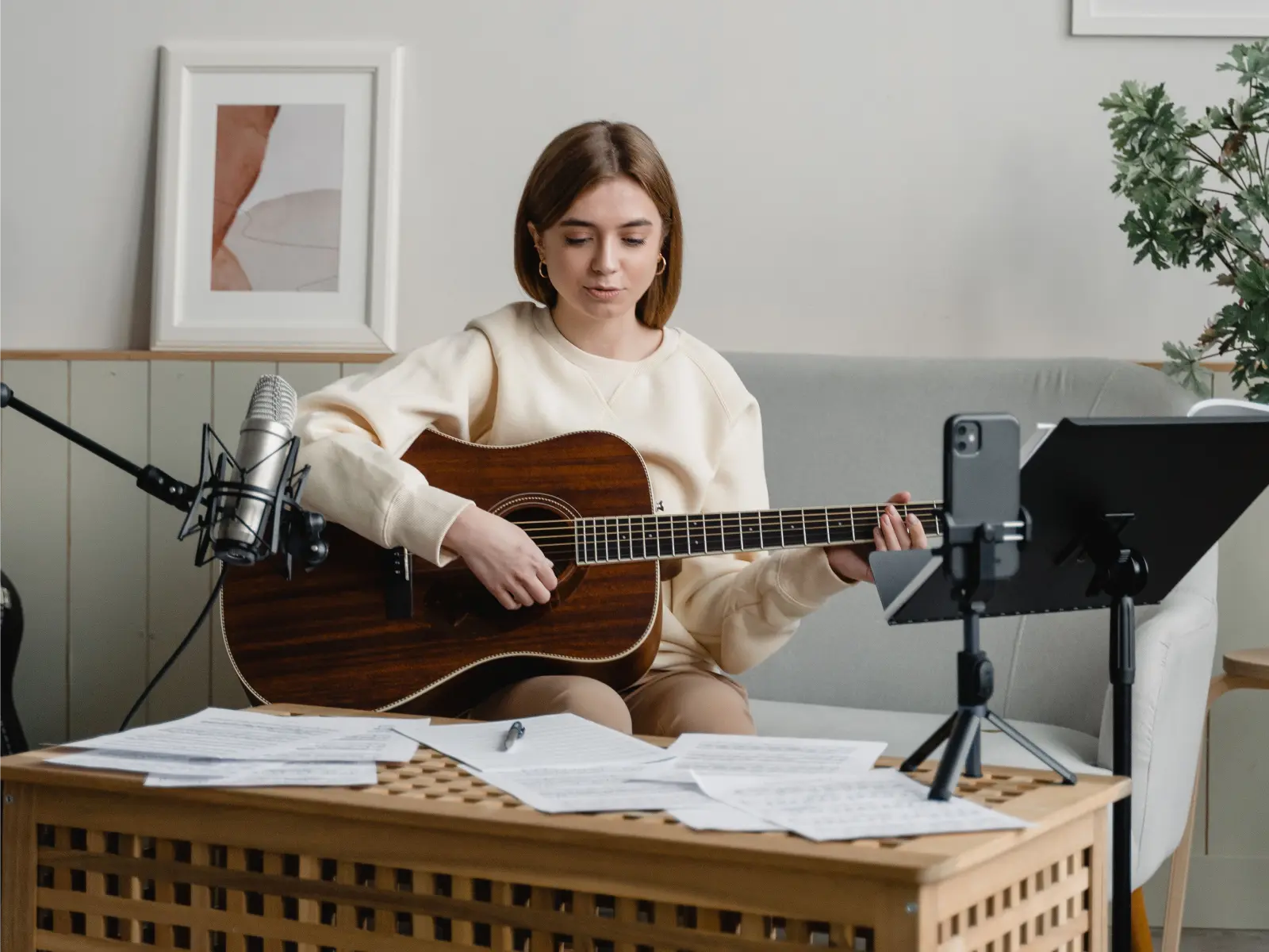 A woman playing an acoustic guitar in a cozy, modern living room setting with music sheets.