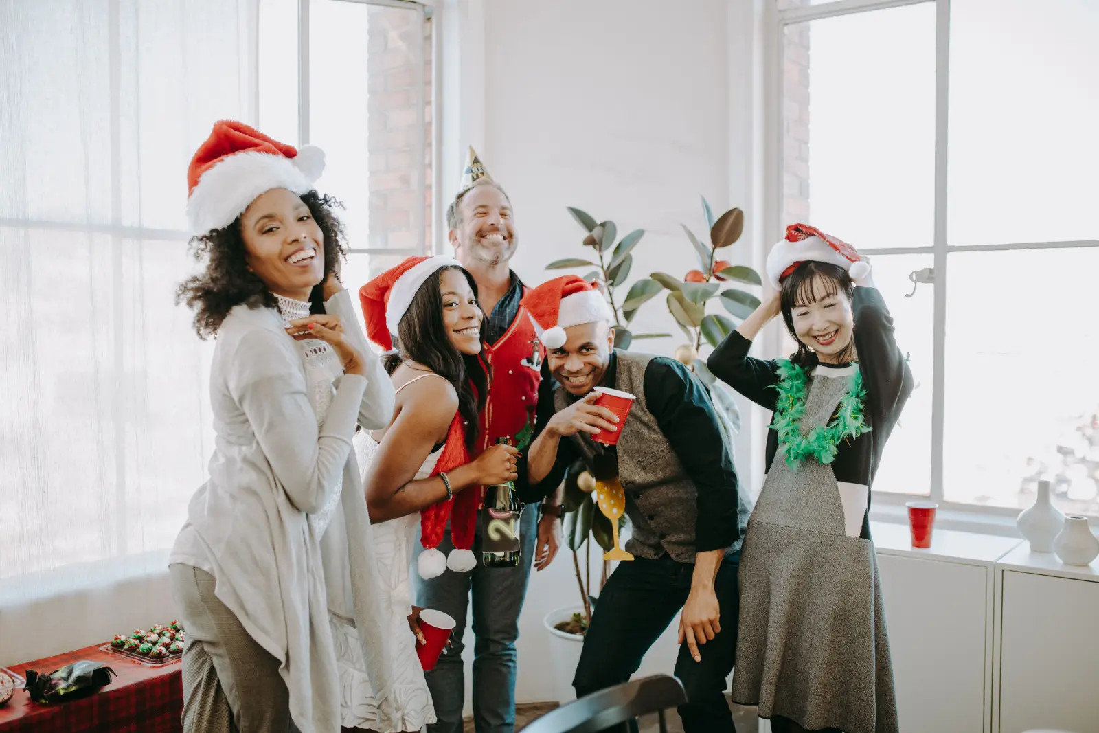 A diverse group of friends celebrating a joyful Christmas party indoors with Santa hats.