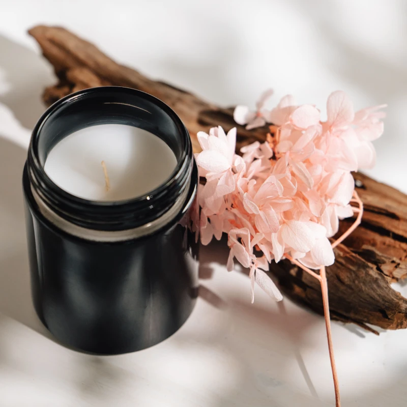 A close-up of a black candle with delicate pink flowers and rustic wood, evoking a serene ambiance.