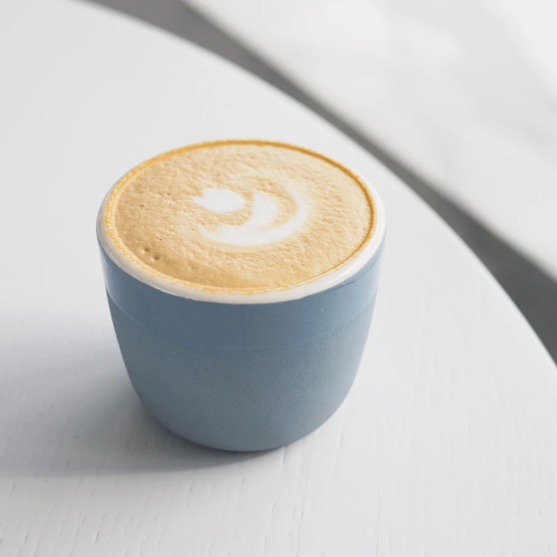 Elegant flat lay of a latte in a blue cup, showcasing intricate latte art on a smooth white surface.