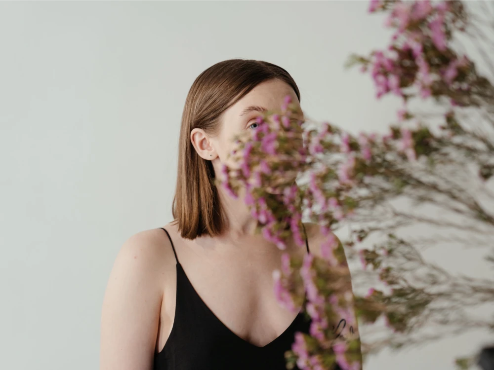 A woman in a black dress partially obscured by pink waxflowers, creating an artistic composition.