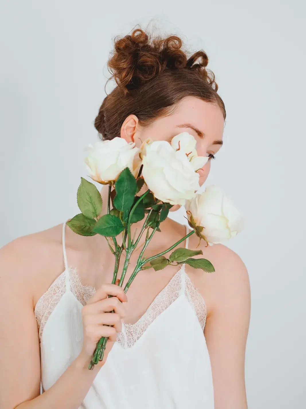 A young woman in a white blouse poses with white roses in a Paris studio setting