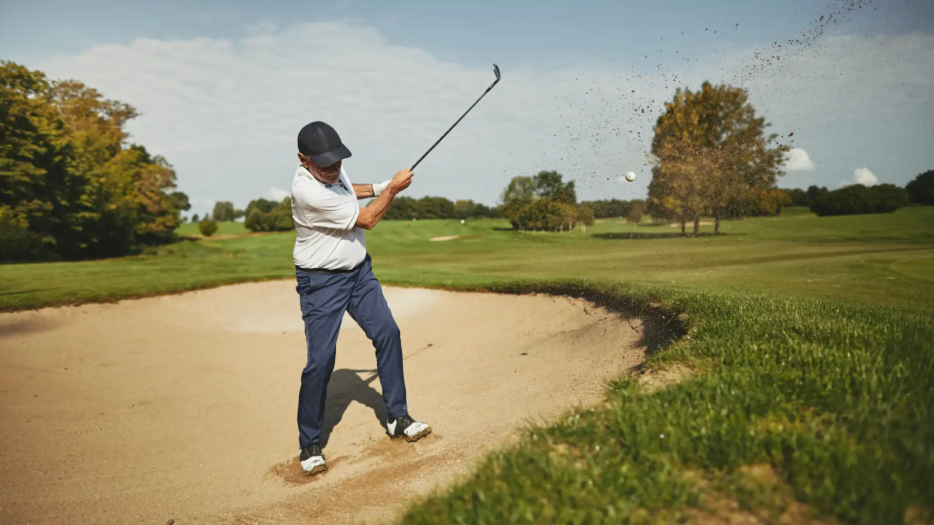 senior man chipping out of a sand trap while